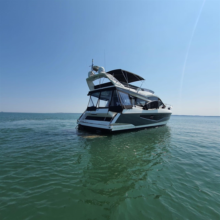 Luxury boat anchored in calm turquoise water under a clear blue sky, showcasing its elegant design and spacious deck.